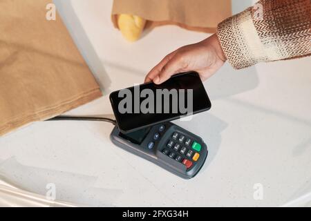 Nahaufnahme einer Frau, die ein Mobiltelefon nutzt und online mit bezahlt Terminal im Shop Stockfoto