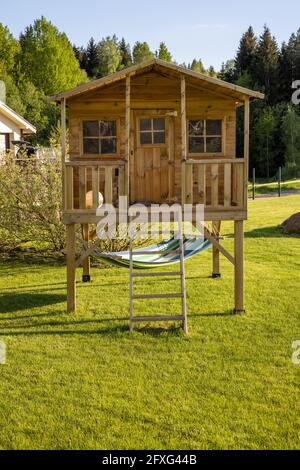Kleines Kinderbaumhaus mit Hängematte im Garten an einem sonnigen Sommertag, warme und gemütliche Umgebung mit Rasen, Spielplatz Stockfoto