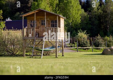 Kleines Kinderbaumhaus mit Hängematte im Garten an einem sonnigen Sommertag, warme und gemütliche Umgebung mit Rasen, Spielplatz Stockfoto