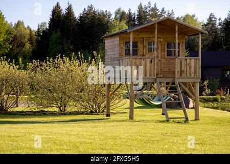 Kleines Kinderbaumhaus mit Hängematte im Garten an einem sonnigen Sommertag, warme und gemütliche Umgebung mit Rasen, Spielplatz Stockfoto