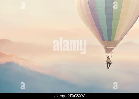 Surreale Frau, die sich auf einer Schaukel genießt, die an einem hängt Heißluftballon Stockfoto