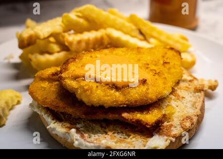 Peri-Peri-Sauce auf einem panierten Hühnchen-Schnitzel, auf einem offenen Brötchen sitzend, mit Käse geröstet, mit knuspriigen Pommes im Hintergrund Stockfoto