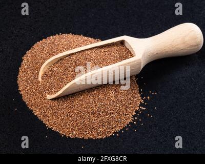 Holzlöffel auf Stapel von Vollkorntaufelsamen auf schwarz Platte Stockfoto