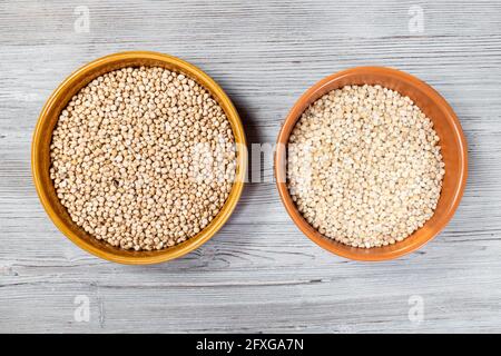 Draufsicht auf ganze und polierte Sorghum-Samen in Runde Keramikschalen auf grauem Holztisch Stockfoto