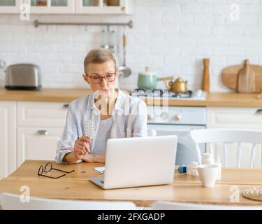 Telemedizin, Videoanruf zum Arzt, Kommunikation mit Medizin online. Moderne fokussierte Frau mittleren Alters mit Online-Anruf auf Laptop zeigt Tabletten in einer Blister. Gesundheits- und Medizinkonzept Stockfoto