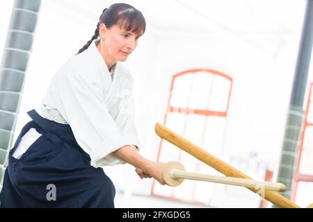 Frau kämpfen mit hölzernen Schwertern an Aikido Training in Martial Arts School Stockfoto