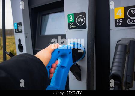 Mann, der ein schnelles EV-Ladegerät von der EV-Ladestation im Fokus hat. Schnelle EV-Ladestation. Laden von Elektrofahrzeugen. Alternative Energie. AC-Kfz-Ladegerät Stockfoto