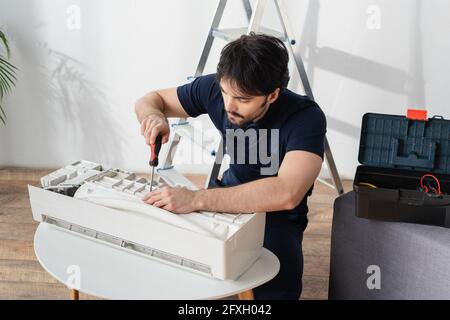 Junger Handwerker in Overalls, der Schraubendreher hält, während er gebrochene Luft repariert Conditioner Stockfoto