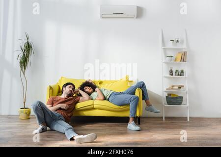 Müdes multiethnisches Paar, das auf dem gelben Sofa sitzt und darunter leidet Hitze im Sommer Stockfoto