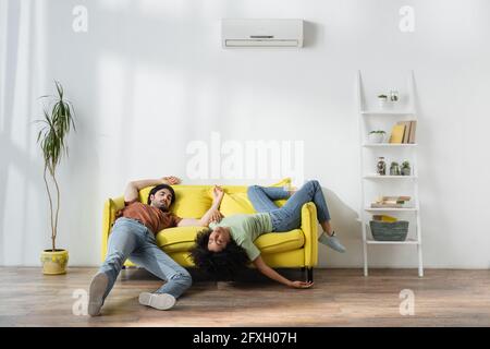 Erschöpfte junge multiethnische Paare liegen auf dem gelben Sofa und leiden Von der Hitze im Sommer Stockfoto