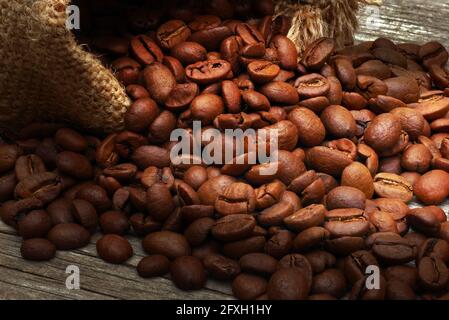 Nahaufnahme von gerösteten Kaffeebohnen, die aus dem Sackleinen verschüttet wurden Holzhintergrund Stockfoto