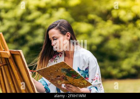 Porträt einer Frau mit einem konzentrierten Expressionsgemälde auf Leinwand in einem Park. Stockfoto