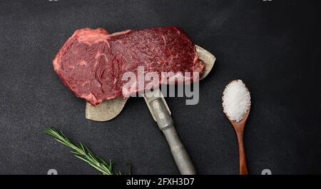 Rohes Stück Rindersteak liegen auf einem Eisenmesser, schwarzer Hintergrund. Klassisches Steak, Blick von oben Stockfoto