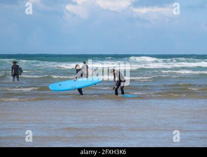 Eine Gruppe junger männlicher Freunde, die ihre gemieteten Surfbretter tragen Zu Fuß ins Meer bei Mawgan Porth zu starten Surfstunde bei einem Aufenthalt in den Cornichern Stockfoto