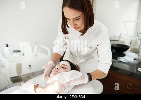 Arzt-Kosmetologe mit Servietten zur Entfernung von Schönheit befeuchten Maske aus dem Gesicht der Frau im Spa-Salon. Hautpflegekonzept Stockfoto