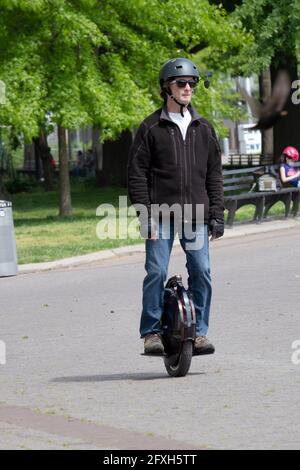 An einem Frühlingstag fährt ein Mann mit einem Hemmchen im Flushing Meadows Corona Park in Queens, New York City, ein Elektro-Einrad. Stockfoto