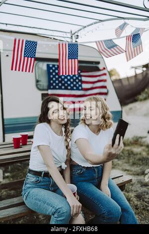Eine schöne Aufnahme von zwei spanischen Frauen, die ein Selfie machen Auf dem Hintergrund der US-Flaggen - Tag der US-Unabhängigkeit Stockfoto