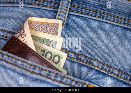 Brieftasche und viele polnische Banknoten ragen aus der Gesäßtasche der Denim-Hose. Foto aufgenommen unter künstlichem, weichem Licht Stockfoto