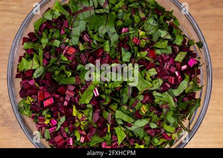 Frische, gehackte Rote-Bete-Blätter in einer Glasschüssel angeordnet. Foto aufgenommen unter künstlichem, weichem Licht. Stockfoto