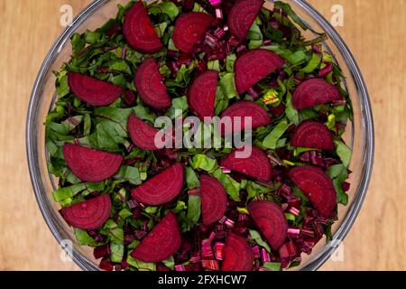 Frische, geschnittene Blätter und Rote Beete in einer Glasschüssel angeordnet. Foto aufgenommen unter künstlichem, weichem Licht. Stockfoto