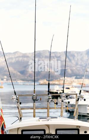 Angelruten, die am Heck einer weißen Yacht vor dem Hintergrund eines Piers, von Booten, Meer und Bergen befestigt sind. Nahaufnahme Stockfoto