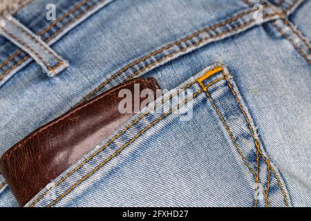 Die Ledertasche ragt aus der Gesäßtasche der Denim-Hose. Foto aufgenommen unter künstlichem, weichem Licht Stockfoto