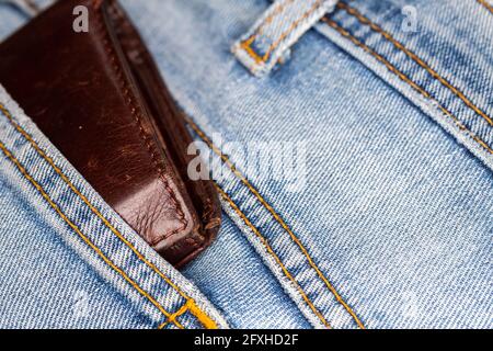 Die Ledertasche ragt aus der Gesäßtasche der Denim-Hose. Foto aufgenommen unter künstlichem, weichem Licht Stockfoto