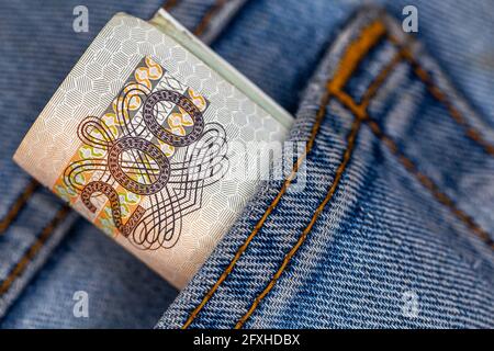 Viele polnische 200-pln-Banknoten ragen aus der Gesäßtasche der Denim-Hose. Foto aufgenommen unter künstlichem, weichem Licht Stockfoto