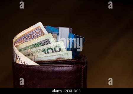 Viele polnische Banknoten und Kreditkarten ragen aus einer braunen Ledertasche. Foto aufgenommen unter künstlichem, weichem Licht Stockfoto