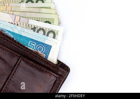 Viele polnische Banknoten ragen aus einer braunen Ledertasche. Foto aufgenommen unter künstlichem, weichem Licht, Objekt isoliert auf weißem Hintergrund Stockfoto