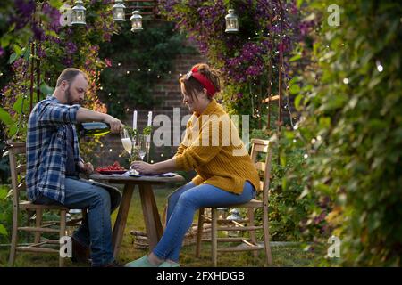 Das Paar genießt Champagner und rote Johannisbeeren am Tisch im Garten Stockfoto