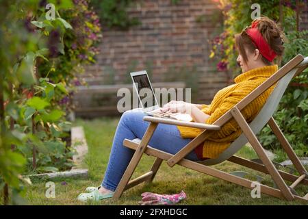 Frau, die im Garten am Laptop arbeitet Stockfoto