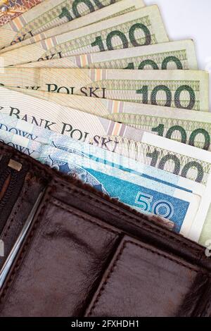 Viele polnische Banknoten ragen aus einer braunen Ledertasche. Foto aufgenommen unter künstlichem, weichem Licht, Objekt isoliert auf weißem Hintergrund Stockfoto