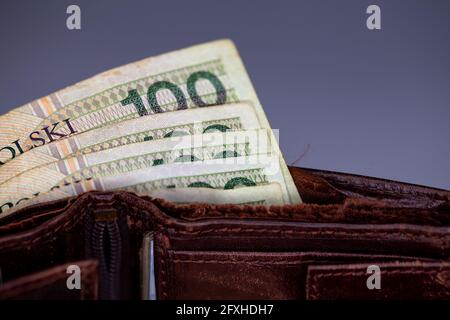 Viele polnische Banknoten ragen aus einer braunen Ledertasche. Foto aufgenommen unter künstlichem, weichem Licht, Grau, verschwommenem Hintergrund. Stockfoto