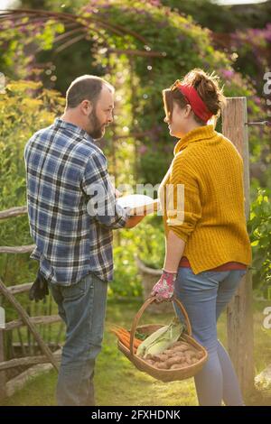 Paar mit Buch und frisch geerntetem Gemüse im Sommergarten Stockfoto