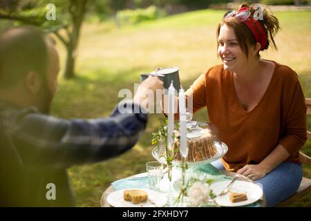 Glückliches Paar, das Tee und Kuchen am Tisch im sonnigen Garten genießt Stockfoto