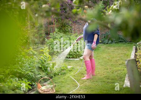 Frau mit Schlauchbewässerung Pflanzen im Sommer Gemüsegarten Stockfoto