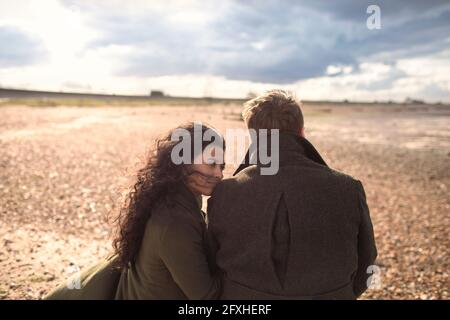 Paar in Mänteln am sonnigen, windigen Winterstrand Stockfoto