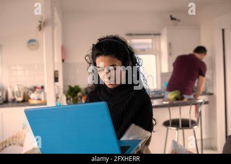 Frau mit Kopfhörern und Laptop, die von zu Hause aus arbeitet Stockfoto