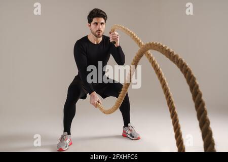 Ein hübscher, athletischer Sportler, der mit isolierten Kampfseilen arbeitet Grauer Hintergrund Stockfoto