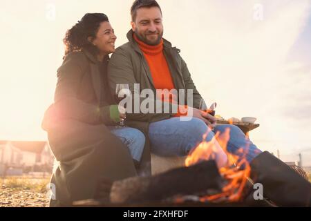 Glückliches Paar, das am Winterstrand Rotwein am Feuer genießt Stockfoto