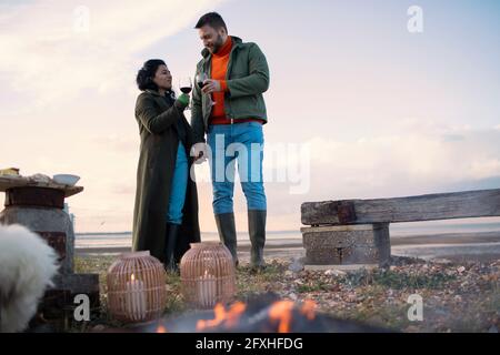 Paar in Wintermänteln genießen Rotwein am Strand Stockfoto