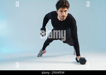 Ein hübscher, athletischer Sportler, der mit über blau isolierten Hanteln trainiert Hintergrund Stockfoto