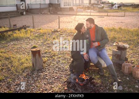 Pärchen in Wintermänteln, die Wein am Kamin auf der Strandterrasse genießen Stockfoto