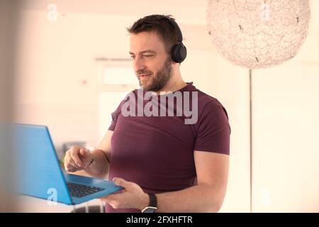 Mann mit Kopfhörern, der von zu Hause aus mit einem Laptop arbeitet Stockfoto