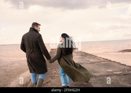 Paar in Wintermänteln, die die Hände am Meeresstrand halten Stockfoto