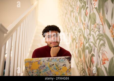 Portrait selbstbewusster junger Mann mit Laptop auf der Treppe zu Hause Stockfoto