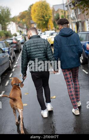 Gay Männlich Paar hält Hände gehen Hund auf nassen Straße Stockfoto