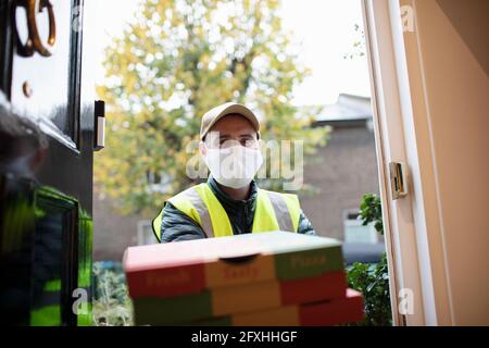 Portrait Delivery Mann in Gesichtsmaske liefern Pizza vor der Haustür Stockfoto