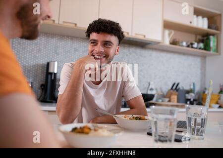Lächelnd schwul männlich paar reden und essen in der Küche Stockfoto
